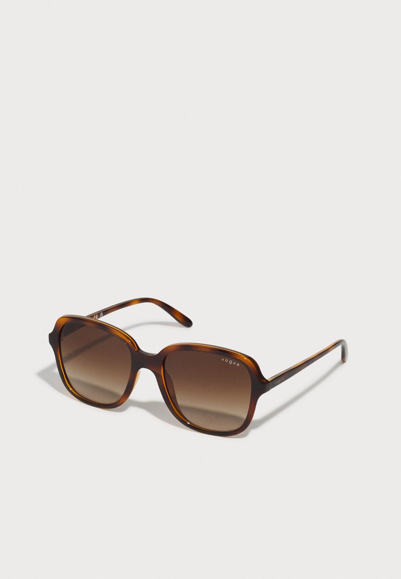 Tortoiseshell sunglasses with an oversized square frame, gradient brown lenses, and the logo "Vogue" printed on the upper left lens.