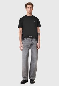 T-shirt nera con scollo rotondo e jeans grigi dal taglio comodo. I dettagli notevoli includono un piccolo logo e una cintura nera con una fibbia argentata.