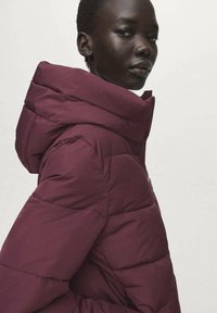 Vínová prošívaná bunda s vysokým límcem a hladkou texturou. Má vodorovné prošívání a zipovou kapsu na boku.