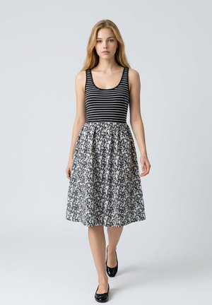 Mujer con camiseta de tirantes a rayas en blanco y negro, falda floral en blanco y negro y bailarinas negras caminando hacia adelante.