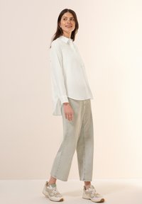 Camicia bianca con bottoni e maniche lunghe, abbinata a jeans larghi grigi chiari e sneakers beige con dettagli verde. Tessuto morbido, vestibilità casual.
