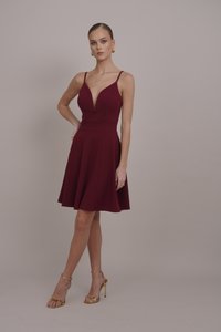 Burgundijas fit-and-flare kleita ar dziļu V-veida kaklu, plāniem siksniņām un krokotu svārku. Saskaņota ar zeltainiem siksnu augstpapēžu zābakiem.