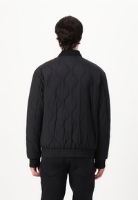 Black quilted bomber jacket featuring a textured wave pattern, ribbed cuffs, and waistband, with a stand-up collar and no visible fastenings.