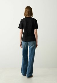 Zwarte katoenen T-shirt met korte mouwen en een ronde hals, gecombineerd met lichtblauwe flared jeans met achterzakken. Eenvoudige, casual look.