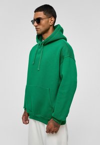 Groene hoodie van zacht materiaal, met een kangoeroezak, verstelbare trekkoordcapuchon en ribgebreide manchetten. Gladde textuur, relaxte pasvorm.