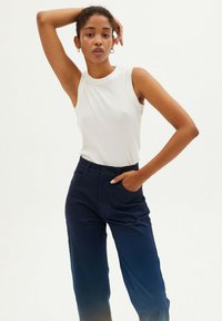 White sleeveless ribbed top paired with dark blue high-waisted trousers, featuring pockets and a front button closure.