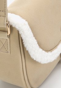 Borsa beige con un morbido bordo in pelliccia bianca, texture liscia, dettagli in metallo dorato e cuciture rinforzate sulla tracolla.