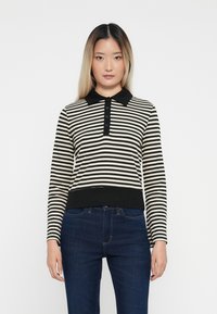 Black and cream striped polo sweater with a collar, featuring a buttoned placket and ribbed cuffs and hem; paired with dark blue jeans.