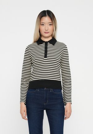 Svart og kremfarget stripete polo genser med krage, som har en knappelukking og ribbestrikkede ermer og hem; kombinert med mørkeblå jeans.