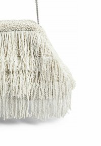Valkoinen fringe-laukkuyhdistää teksturoitua kangasta, ketjuhihnan ja rakenteellisen muodon. Koristeltu pitkillä, roikkuvilla materiaalisuikaleilla.