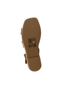 Semelle extérieure en cuir marron avec un dessous en caoutchouc beige lisse, comportant une étiquette d'instructions d'entretien imprimée et une forme plate et arrondie.