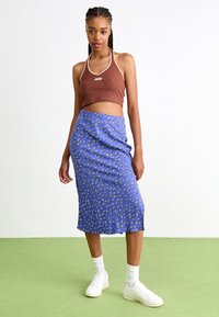 Top scurt cu dungi maro și guler halter, asortat cu o fustă midi cu model floral albastru. Adidași albi și șosete albe cu dungi finalizează ținuta.