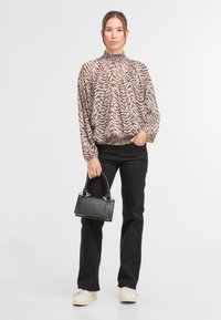 Długo rękawowa, jasnobrązowa bluzka w czarne paski tygrysa, z marszczoną dekoltem i dołem, zestawiona z czarnymi spodniami w stylu dzwonów oraz małą czarną torebką.