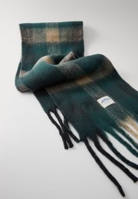 Bufanda de lana con un patrón de cuadros en verde y negro, con bordes con flecos y una etiqueta que muestra los detalles de la marca. Acabado suave y texturizado.