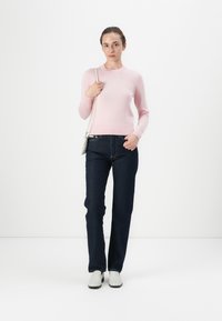 Maglione lavorato a maglia rosa chiaro, aderente con maniche lunghe. Jeans dritti blu scuro. Stivaletti bianchi alla caviglia. La modella tiene una piccola borsa a tracolla argentata.