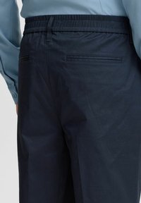 Navy blue, elastic waistband pants featuring a smooth texture, with two back pockets having horizontal seams for subtle detailing.