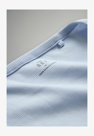 Lichtblauw geribd stof met een getextureerd oppervlak; bevat een label met de tekst "THE SET M" en "MADE IN BANGLADESH" nabij de geribbelde halslijn.