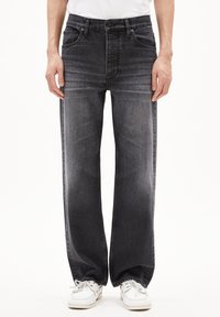 Wijde denimjeans in een donkergrijze wassing, met subtiele vervaging, vijf zakken en een klassieke knoop- en rits sluiting. Gecombineerd met witte schoenen.