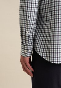 Camicia con bottoni in un motivo a quadri verde e blu navy, con colletto e dettagli sui polsini. Il tessuto appare liscio con una vestibilità strutturata.