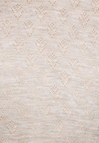 Svijetlo bež pleteni materijal otvorenog uzorka u obliku dijamanta. Meka tekstura s ravnomjerno raspoređenim ukrasnim rupicama diljem tkanine.