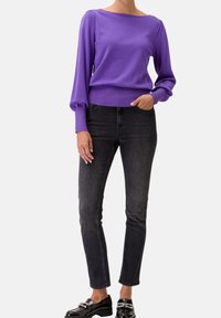 Pull violet avec un décolleté bateau, des manches longues froncées et un ourlet ajusté, associé à un jean skinny noir foncé et des chaussures noires brillantes.