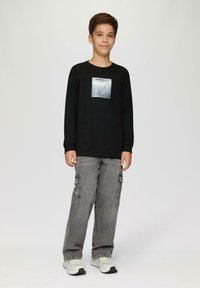 Zwarte lange mouwen shirt met een zilveren grafiek op de borst, gecombineerd met grijze cargobroeken en lichte sneakers. Eenvoudig, casual ontwerp.