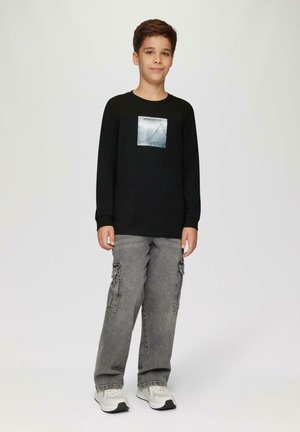 Zwarte lange mouwen shirt met een zilveren grafiek op de borst, gecombineerd met grijze cargobroeken en lichte sneakers. Eenvoudig, casual ontwerp.