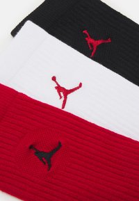Drie geribbelde haarbanden in zwart, wit en rood, elk voorzien van geborduurde Jumpman-logo's in bijpassende kleuren op elke band.