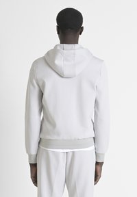Felpa grigia chiara con cappuccio regolabile, polsini e orlo a costine. Tessuto morbido al tatto, design minimalista e senza loghi o motivi visibili.