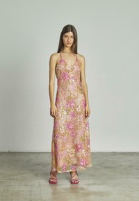 Abito lungo con ricamo floreale rosa e paillettes. Spalline sottili, corpino aderente e gonna fluida. Indossato con tacchi a strappo rosa.