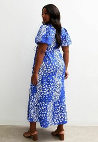 Blå blommig maxikjol med puffärmar och en flerradig design, med vita blommönster och en samlad midja. Bruna klacksandaler.