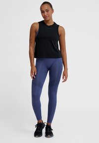 Schwarzes ärmelloses Oberteil mit rundem Halsausschnitt, kombiniert mit figurbetonten navy Leggings mit strukturierten Akzenten und hoher Taille. Schwarze Sneakers runden den Look ab.