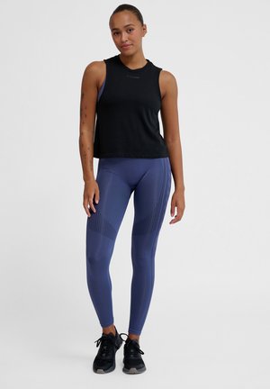 Black sleeveless top with a rounded neckline, paired with fitted navy leggings featuring textured accents and a high waist. Black sneakers complete the look.