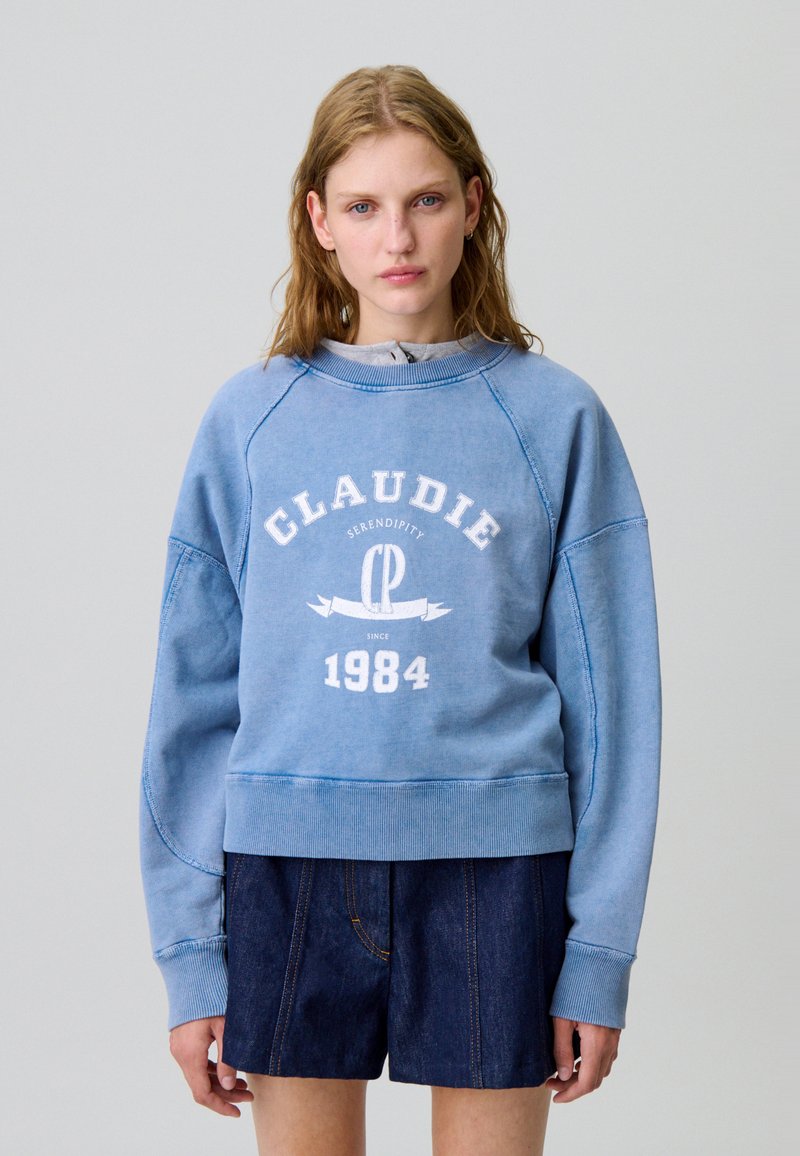 Felpa in cotone blu chiaro con maniche raglan, caratterizzata da un logo bianco e dall'anno "1984". Abbinata a pantaloni corto in denim scuro, design semplice.