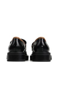 Para czarnych i brązowych skórzanych eleganckich butów widzianych od tyłu z grubymi czarnymi podeszwami i niskimi obcasami na białym tle.