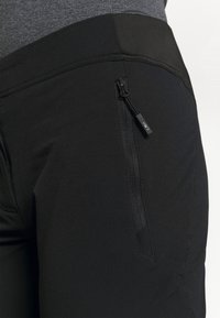 Mustat joustavat housut, joissa on sivussa vetoketjullinen tasku, sileä pinta ja istuva malli, ihanteelliset urheilukäyttöön.