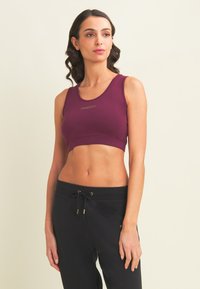 Sujetador deportivo burdeos con escote redondo y diseño ajustado. Presenta un sutil logo dorado en el centro. Tejido suave y elástico.