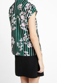 Kortsleeve topp med ett svart och grönt randigt mönster och vita blommor, gjord av lättviktig tyg, med en lös passform.