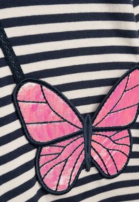 Gestreifter Stoff in Marineblau und Weiß mit einem applizierten rosa Schmetterlingspatch, der glänzende Akzente und gestickte schwarze Umrisse aufweist.
