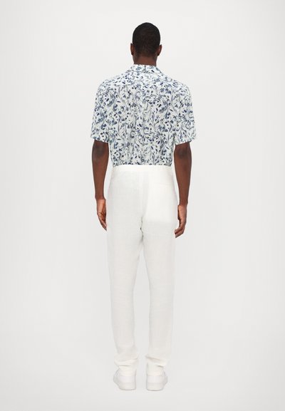 Korte mouwen bloemenhemel in lichtblauw en wit, gecombineerd met witte linnen broek en witte sneakers. Casual, relaxte pasvorm.