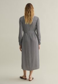 Long-sleeve, black and white polka dot dress, with a fitted waist and flowy skirt. Worn with black sandals featuring a gold accent.