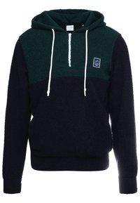 Pull à capuche en tissu doux et duveteux avec un design bloc de couleurs en bleu foncé et vert. Présente un zip sur le devant à mi-hauteur et des cordons de serrage blancs.