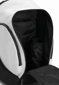 Svart och vit ryggsäck med en stor öppning, har flera interna fickor och ett mjukt tygfoder. Dragkedja synlig.