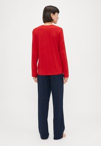 Rotes Langarmshirt mit rundem Ausschnitt, kombiniert mit navyfarbenen Hosen mit einem mehrfarbigen Punktmuster. Aus weichem Stoff gefertigt.