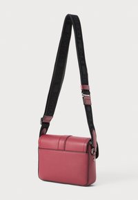 Rosa läder crossbody-väska med en strukturerad form, som har en dubbelficka-design och en svart justerbar rem med präglad logotyp.