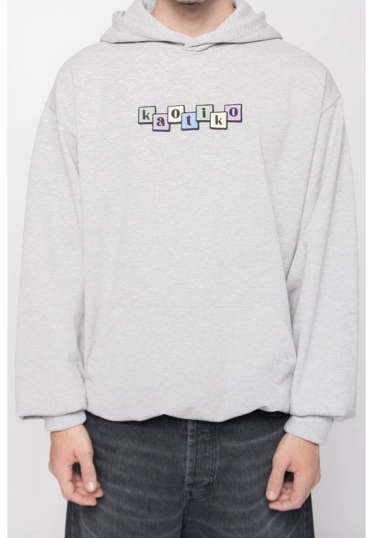 Sweat à capuche gris clair avec des lettres colorées en blocs formant le mot « kaotiko » sur la poitrine, porté avec un jean foncé.