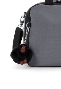 Grå tekstil skuldertaske med sorte accenter, udstyret med en fuzzy sort gorilla nøglering fastgjort til en sølvkæde.