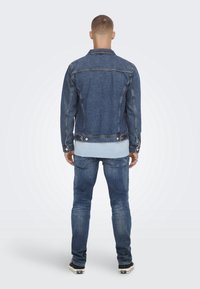 Tummansinisestä farkkutakista, jossa on hieman kulunut pinta, löytyy metalliosia ja vaaleansiniset ribbihaitarit. Takki yhdistettyinä samansävyisiin farkkuihin.