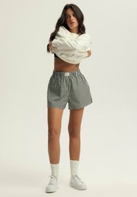 Czarno-białe spodenki w kratę typu gingham z elastycznym pasem, zestawione z luźną białą bluzką i białymi trampkami, z teksturowanymi skarpetkami do kostek.