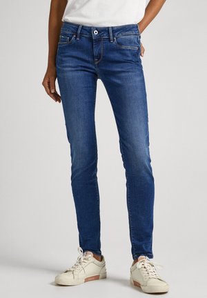 Jeans ajustados de color azul hechos de denim, con una cintura de altura media, cinco bolsillos y costuras en contraste, combinados con zapatillas beige.